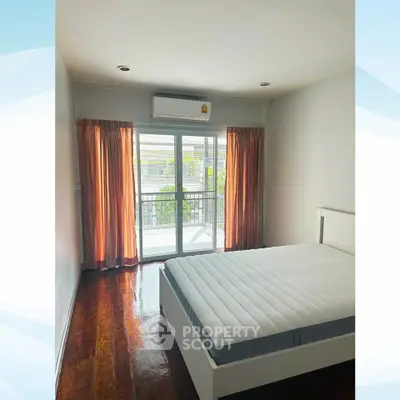 Spacious bedroom with large window and balcony access, featuring polished wooden floors and modern air conditioning.