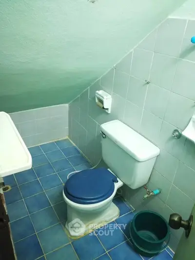 Compact bathroom with blue tiles and sloped ceiling, featuring a toilet and sink.