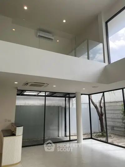 Spacious modern living room with high ceilings and large windows offering natural light and outdoor views.
