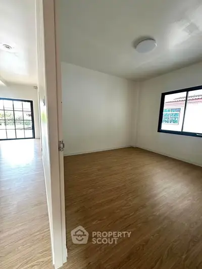 Spacious empty room with wooden flooring and large window, perfect for customization.