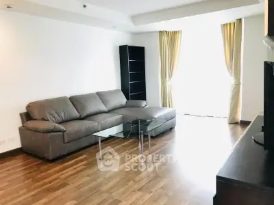 Spacious living room with modern sofa and glass coffee table, featuring elegant wooden flooring and natural light.