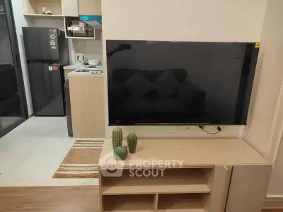 Modern living room with sleek TV setup and stylish kitchen in open layout apartment.