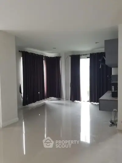 Spacious living room with glossy floors and large windows with dark curtains.