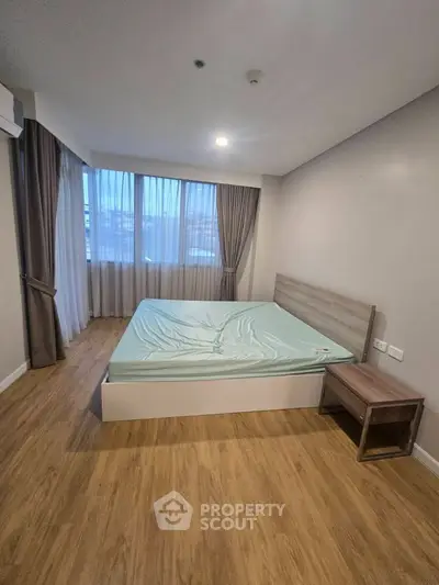 Spacious bedroom with large windows and wooden flooring in modern apartment