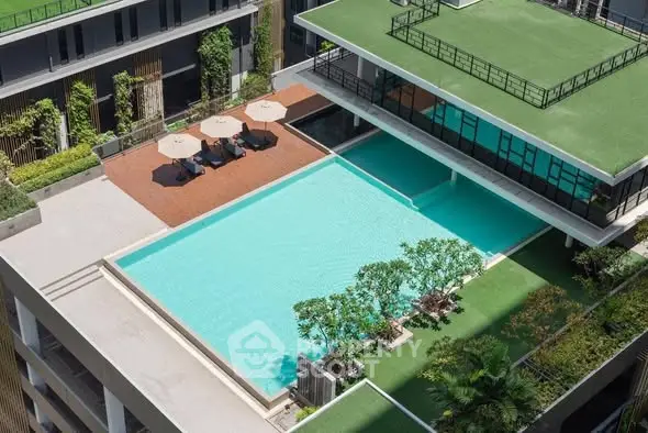 Luxurious rooftop pool with sun loungers and greenery in modern apartment complex.