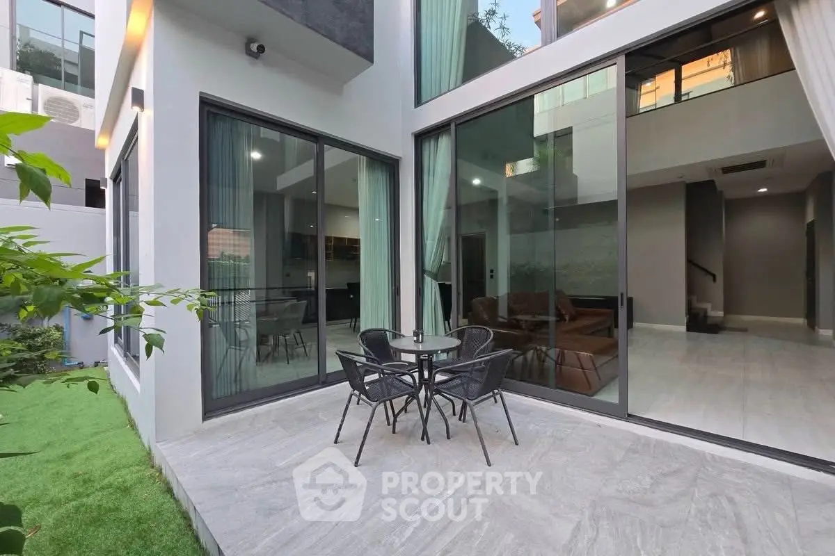 Modern home exterior with large glass doors and cozy patio seating area.