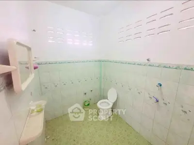 Spacious bathroom with tiled walls and floor, featuring a toilet and mirror, ideal for renovation.