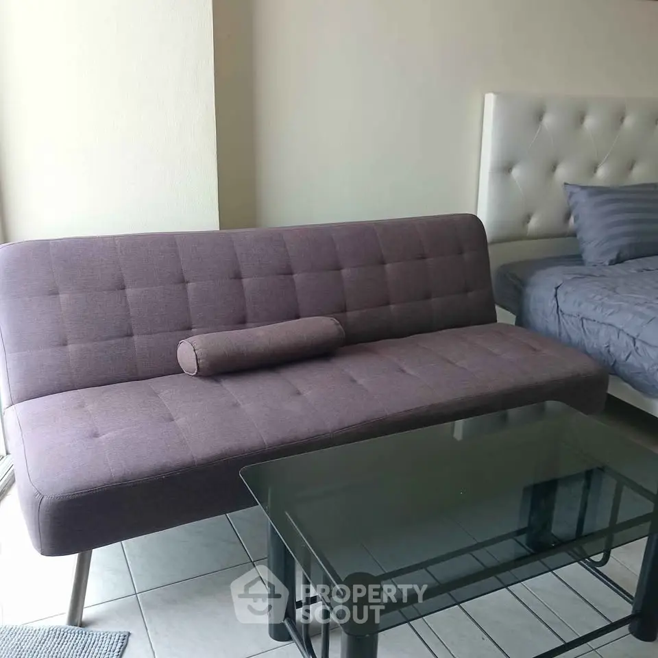 Modern studio apartment with stylish sofa and glass coffee table next to a cozy bed.