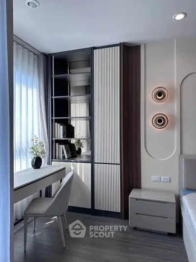 Modern study room with sleek desk, chair, and built-in shelving, featuring stylish wall lighting and large window.