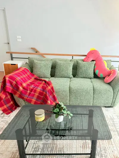 Stylish living room with modern green sofa and glass coffee table, accented by a playful pink dinosaur pillow.