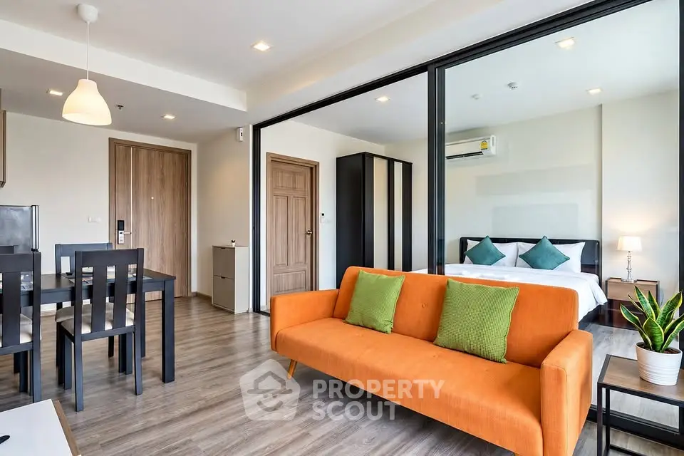 Modern open-plan living room with vibrant orange sofa and stylish bedroom view.