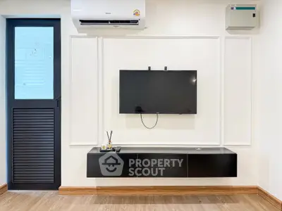 Modern living room with wall-mounted TV and sleek black console under air conditioning unit.