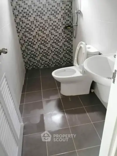 Modern bathroom with tiled walls and floor, featuring a toilet and sink.