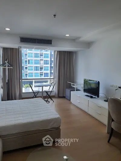 Modern studio apartment with large windows and city view, featuring a cozy bed and compact dining area.