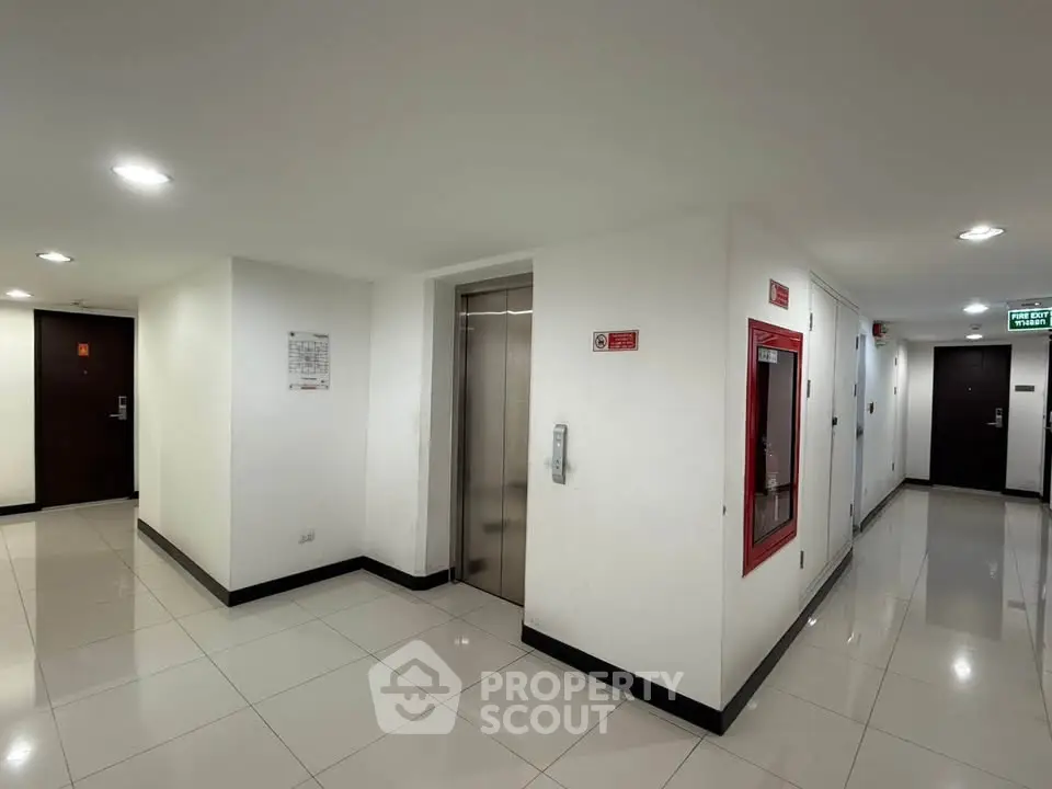 Modern apartment building corridor with elevator and emergency equipment.