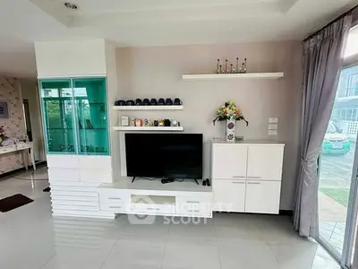 Modern living room with sleek white furniture and large TV, featuring a glass display cabinet and decorative shelves.