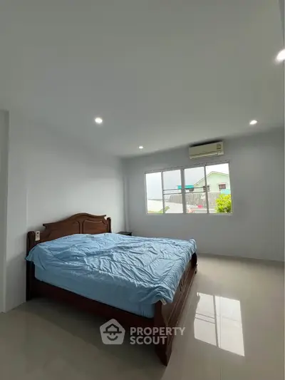 Spacious bedroom with large window and natural light, featuring a wooden bed and modern air conditioning.