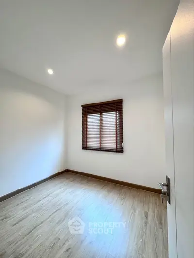 Spacious empty room with wooden flooring and window blinds, perfect for customization.