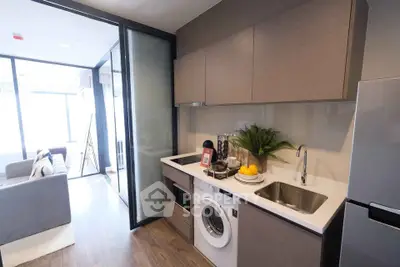 Modern kitchen with sleek cabinetry, washing machine, and open layout leading to a bright living area.