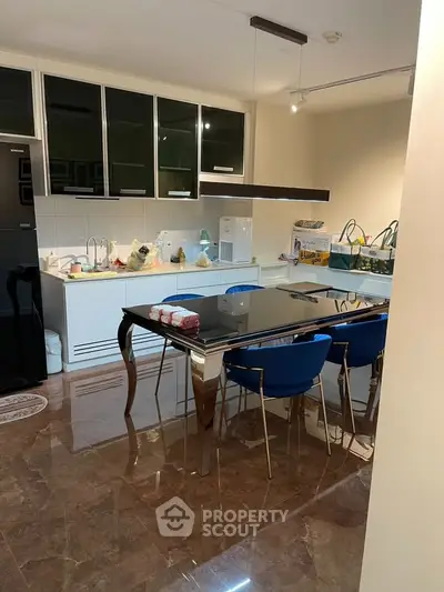 Modern kitchen with sleek black dining table and blue chairs, featuring glossy cabinets and marble flooring.