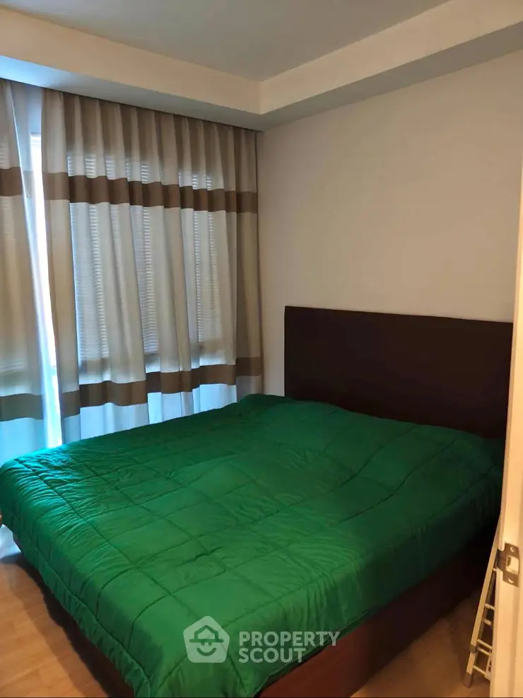 Cozy bedroom with green bedding and large window with curtains