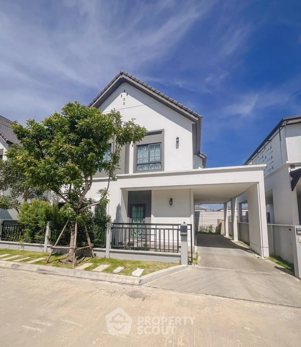Modern two-story house with driveway and lush greenery under a clear blue sky.