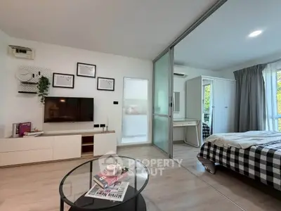 Modern living room with glass partition leading to a cozy bedroom, featuring stylish decor and natural light.