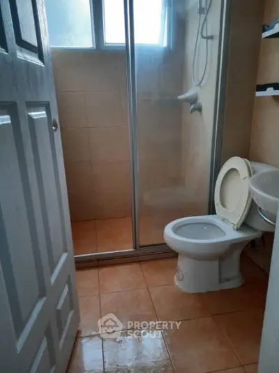 Compact bathroom with shower and toilet, tiled floor, and natural light from window.