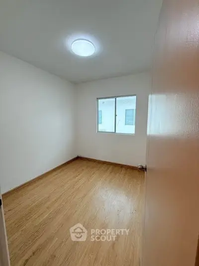 Spacious empty room with wooden flooring and bright window, perfect for customization.