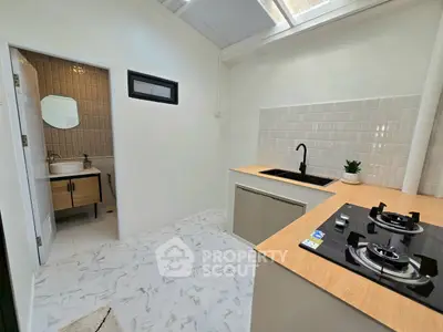 Modern kitchen with gas stove and adjacent bathroom, featuring sleek design and natural lighting.