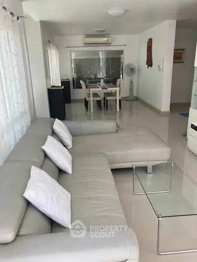 Spacious modern living room with elegant white sofa and glass coffee table, leading to a stylish dining area.