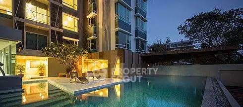 Luxurious apartment building with illuminated poolside at dusk, offering serene ambiance and modern architecture.