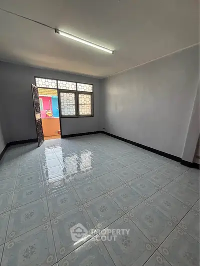 Spacious empty room with tiled flooring and large window, ideal for customization.