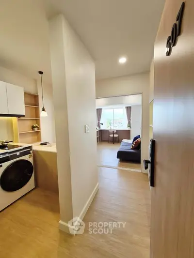 Modern apartment entrance with open kitchen and cozy living area, featuring sleek design and natural light.