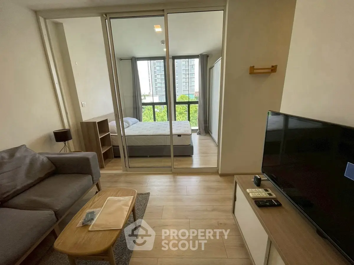 Modern living room with cozy sofa and TV, adjacent to a bright bedroom with large windows.