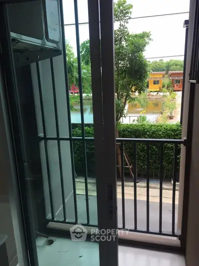 Charming balcony view with lush greenery and colorful houses by a serene pond.