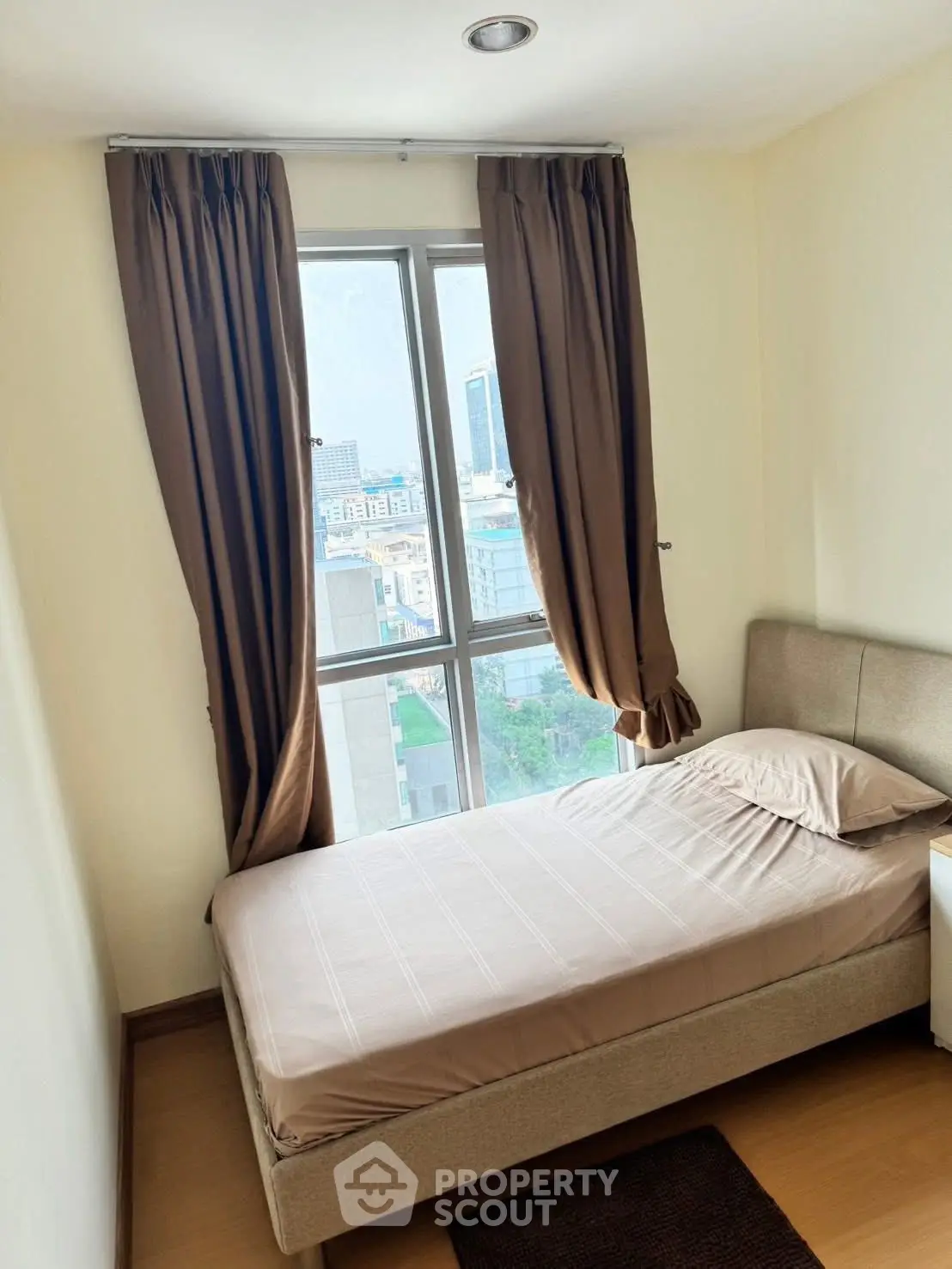 Cozy bedroom with a single bed and large window offering city views, perfect for urban living.
