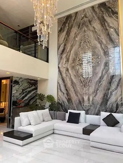 Luxurious living room with high ceiling, elegant chandelier, and stunning marble accent wall.