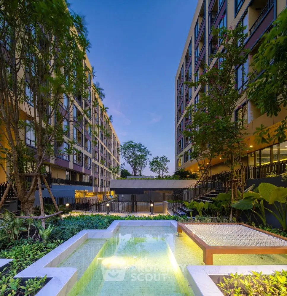 Modern apartment complex with lush garden and serene pool area at dusk.