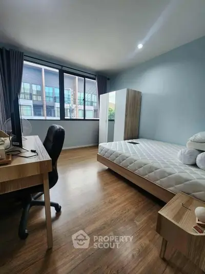 Modern bedroom with large window and wooden flooring, featuring a desk and bed.
