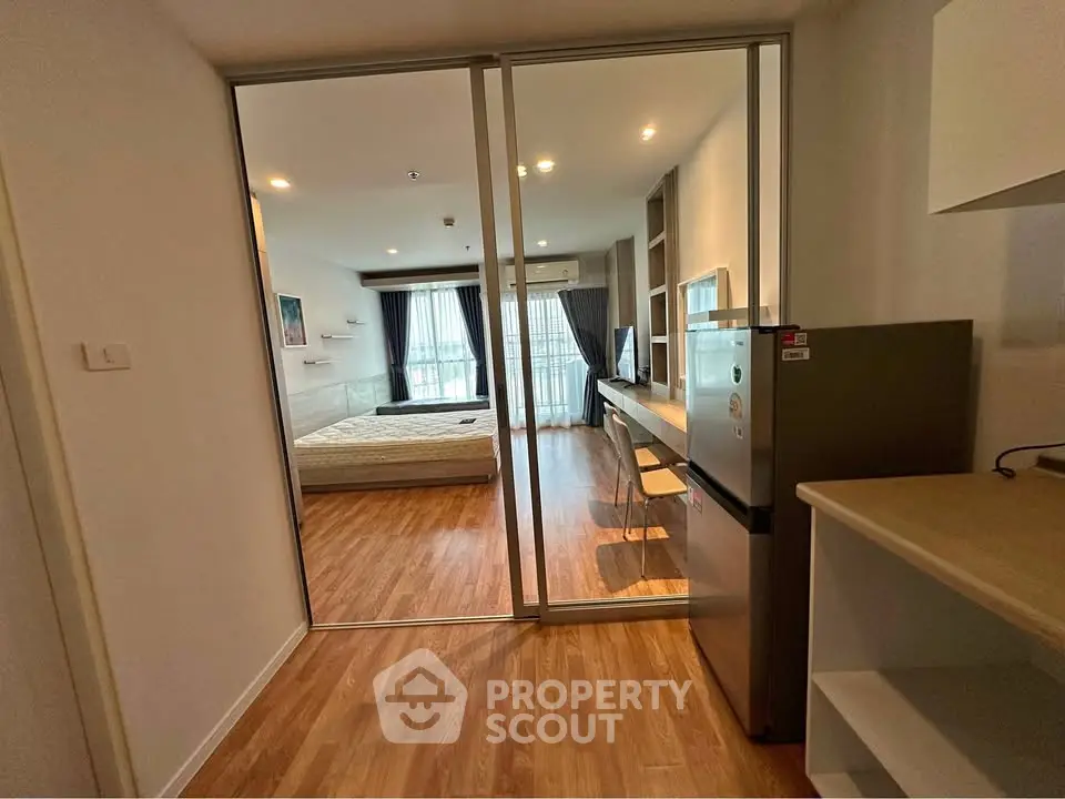 Modern studio apartment with wooden flooring and glass partition, featuring a cozy bedroom and compact kitchen.