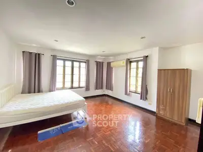 Spacious bedroom with wooden flooring and large windows for natural light.