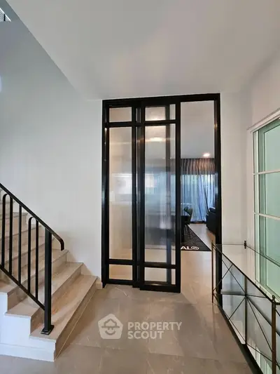 Modern interior with stylish staircase and glass partition leading to a cozy living area.