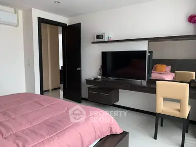 Modern bedroom with sleek furniture and wall-mounted TV, featuring a cozy pink bedspread.