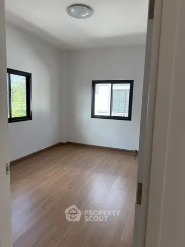 Spacious empty bedroom with wooden flooring and large windows for natural light.