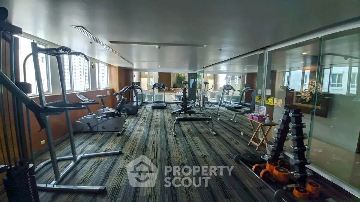 Spacious gym with modern equipment and large windows in a luxury building.