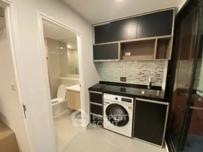 Modern apartment with sleek kitchen and adjacent bathroom, featuring stylish cabinetry and a washing machine.
