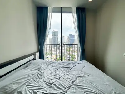 Modern bedroom with city view from large window, featuring elegant curtains and cozy bedding.