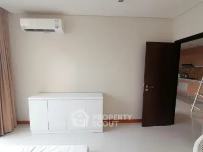 Modern bedroom with air conditioning and sleek white furniture, offering a glimpse into a stylish kitchen.