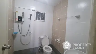 Compact bathroom with wall-mounted shower, toilet, and small window for natural light, tiled for easy maintenance.